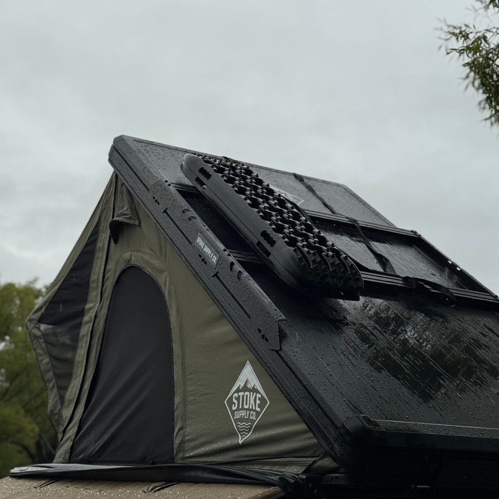 Traction boards carried on Stoke slimline crossbars on top of a green hard-shell rooftop tent