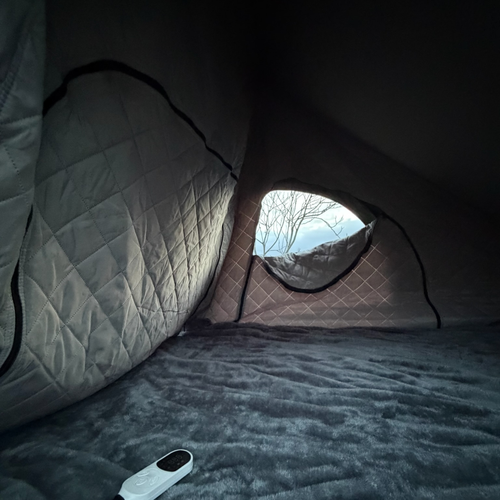 Stoke Electric Blanket XL laid over the mattress inside a rooftop tent, white controller on the plush grey blanket, window at right