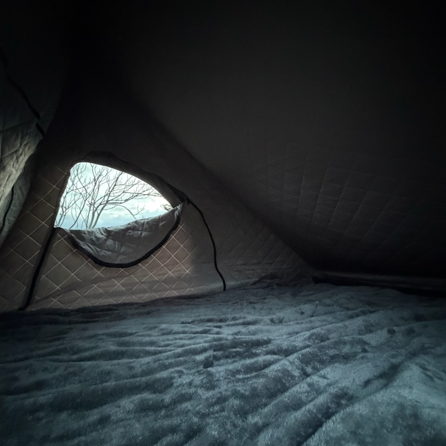 Warm insulated interior of a Stoke rooftop tent at night, quilted liner and mattress with a window view