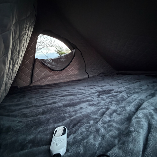 Plush grey Stoke Electric Blanket XL covering a rooftop tent mattress, digital controller resting on top
