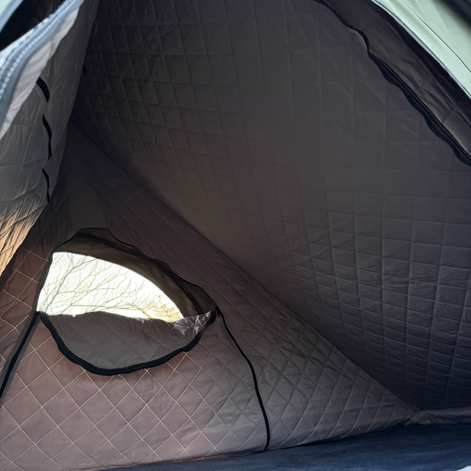 Inside a Stoke rooftop tent fitted with the quilted insulation liner across the ceiling and walls, window at left